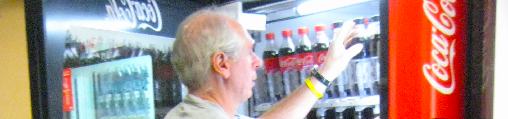 A close up of a man restocking an open vending machine of coca-cola.