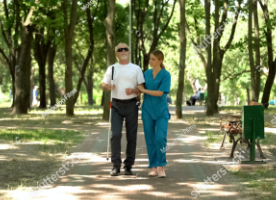 Picture of A healthcare worker guiding a blind man through a park.